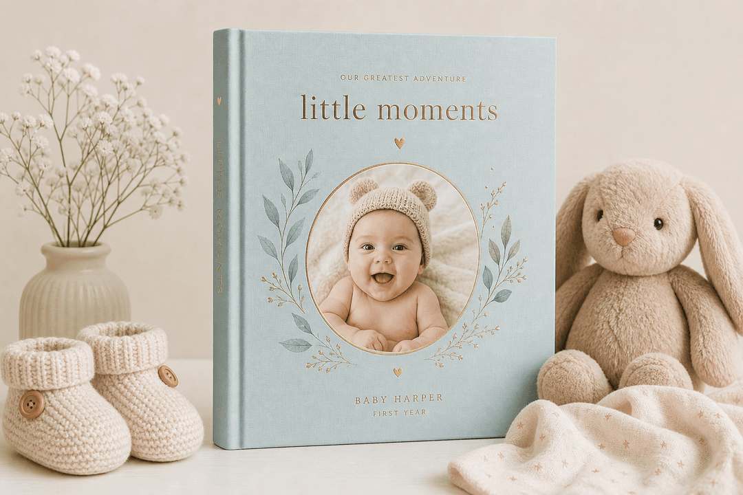 Illustration of a premium hardcover baby photo book beside baby booties and plush toy